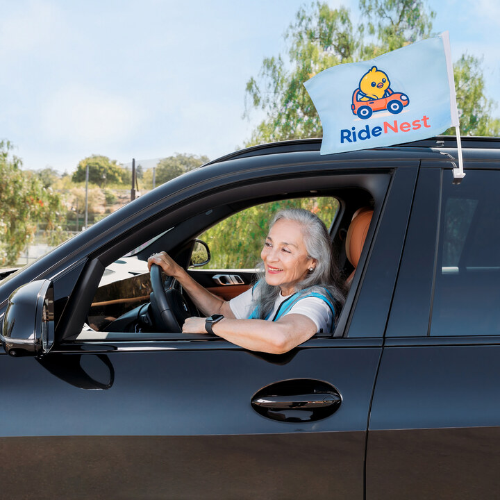 Uniformed older adult waving from a branded black SUV.