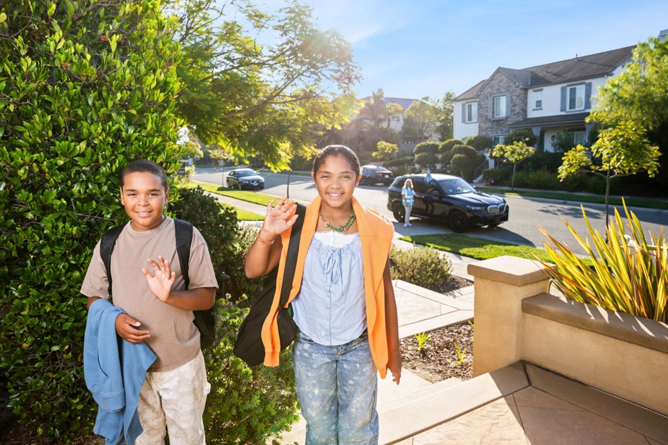 Two backpacked youths on a residential walk; vehicle in background.